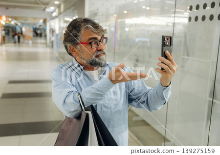 Usage of the smartphone. Senior man is in the mall, shopping time conception Usage of the smartphone. Senior man is in the mall, shopping time conception 139275159