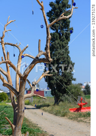 Colorful glass ornaments hang from a rustic tree on a sunny day in an open field, with vibrant greenery around and a distant red canoe visible Colorful glass ornaments hang from a rustic tree on a sunny day in an open field, with vibrant greenery around and a distant red canoe visible 139275178