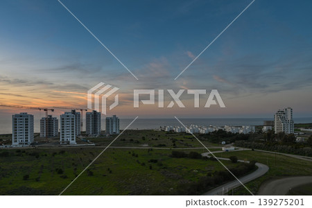 Coastal sunset illuminates modern buildings along the shoreline at dusk 139275201
