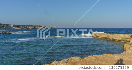 Tranquil coastal view at sunset with gentle waves lapping against rocky shores. Tranquil coastal view at sunset with gentle waves lapping against rocky shores. 139275359