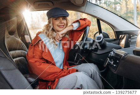 On the steering wheel, resting. Happy blonde woman is sitting her electric car On the steering wheel, resting. Happy blonde woman is sitting her electric car 139275677