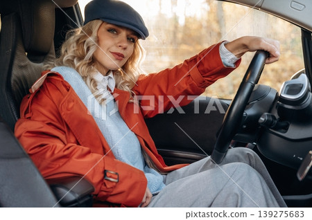 In red coat and blue beret. Happy blonde woman is sitting her electric car 139275683