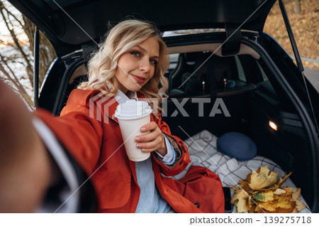 Selfie time. Positive facial expression. Beautiful blonde woman is with her blue electric car on the road of forest Selfie time. Positive facial expression. Beautiful blonde woman is with her blue electric car on the road of forest 139275718