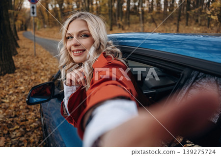 Selfie time. Positive facial expression. Beautiful blonde woman is with her blue electric car on the road of forest 139275724
