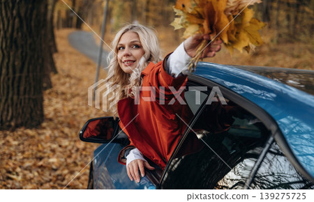 Beautiful blonde woman is with her blue electric car on the road of forest 139275725