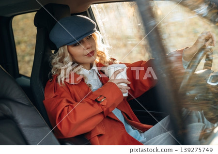 Hot drink in white cup. Happy blonde woman is sitting her electric car 139275749