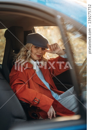 In red coat and blue beret. Happy blonde woman is sitting her electric car In red coat and blue beret. Happy blonde woman is sitting her electric car 139275752