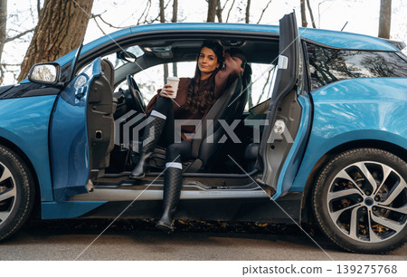 On the road, door opened, parked. Beautiful woman is sitting in her electric car On the road, door opened, parked. Beautiful woman is sitting in her electric car 139275768