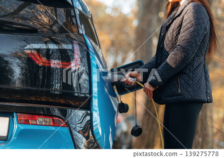 Close up view of woman that is putting charger into the electric car outdoors 139275778