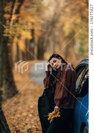 Woman is outdoors near her electric blue car at daytime, rural scene 139275827