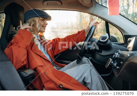 View from the side. Happy blonde woman is sitting her electric car View from the side. Happy blonde woman is sitting her electric car 139275870