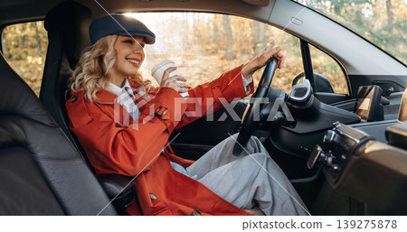 Coffee break, enjoying the drink. Happy blonde woman is sitting her electric car Coffee break, enjoying the drink. Happy blonde woman is sitting her electric car 139275878