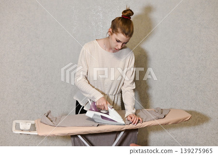 Woman ironing clothes in a room with patterned wall Woman ironing clothes in a room with patterned wall 139275965