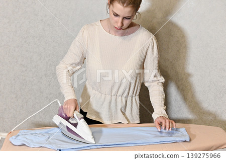 Woman ironing clothes in a room with patterned wall 139275966