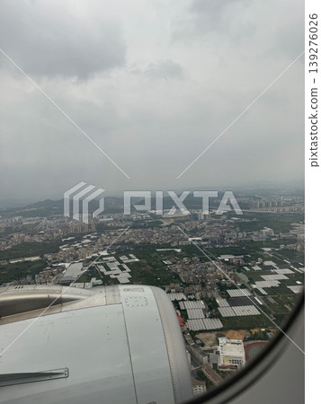 Aerial city view from airplane window over cloudy sky and aircraft engine, urban landscape with fields and buildings under overcast weather Aerial city view from airplane window over cloudy sky and aircraft engine, urban landscape with fields and buildings under overcast weather 139276026