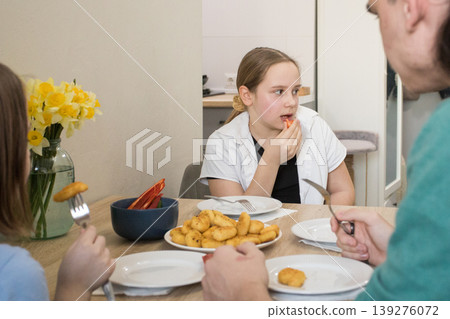 A group of four family members sits at a table together. A group of four family members sits at a table together. 139276072