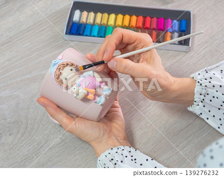 Hands gently paint a polymer clay figurine with soft colors. Close up 139276232