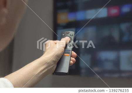 Hand holds remote, aiming at glowing TV screen. Smart TV. Hand holds remote, aiming at glowing TV screen. Smart TV. 139276235
