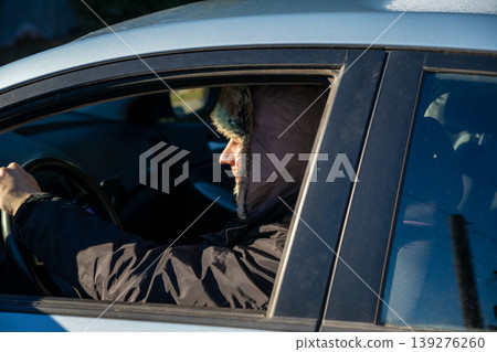 Man driver in winter hat driving car. Delivery worker during cold season. Transportation service or taxi driver on city road. Safe travel and professional vehicle operation in wintertime. Man driver in winter hat driving car. Delivery worker during cold season. Transportation service or taxi driver on city road. Safe travel and professional vehicle operation in wintertime. 139276260