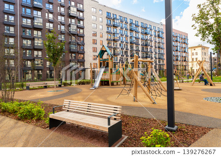 Modern playground in residential district. Wooden jungle gym with slide and climbing net in backyard of building complex. Architecture of urban area for recreation and childhood activity. Modern playground in residential district. Wooden jungle gym with slide and climbing net in backyard of building complex. Architecture of urban area for recreation and childhood activity. 139276267