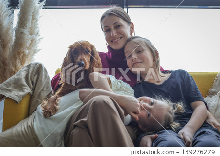 Joyful mother and children sitting on couch with his puppy dog pet. Loving family at home Joyful mother and children sitting on couch with his puppy dog pet. Loving family at home 139276279