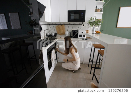 Beautiful woman opening oven in modern kitchen indoor Beautiful woman opening oven in modern kitchen indoor 139276296