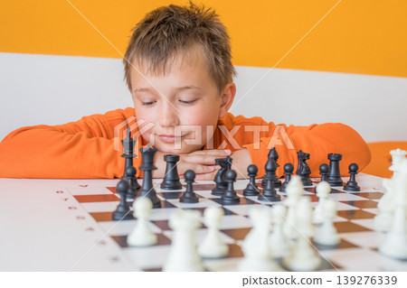 Cute child boy playing chess at school indoors Cute child boy playing chess at school indoors 139276339