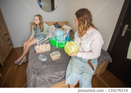 Mom and girl sit on a bed in a small room with pet. Mom and girl sit on a bed in a small room with pet. 139276534