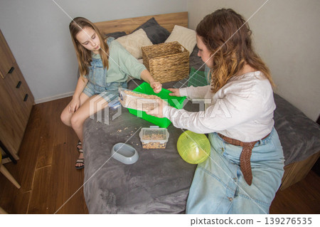 Mom and girl sit on a bed in a small room with pet. Mom and girl sit on a bed in a small room with pet. 139276535