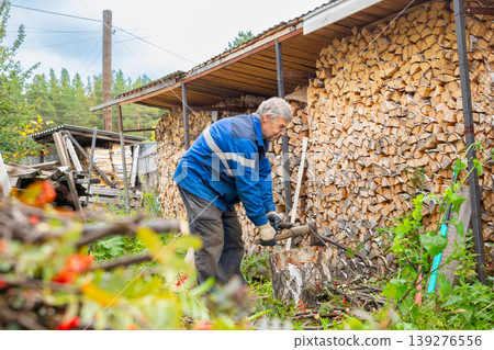 Lumberjack chopping branch with axe near wood stack. Mature man preparing firewood for winter. Manual labor in rural backyard. Traditional worker harvesting fuel for heating home. Lumberjack chopping branch with axe near wood stack. Mature man preparing firewood for winter. Manual labor in rural backyard. Traditional worker harvesting fuel for heating home. 139276556