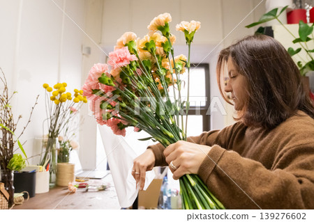 Woman florist wrapping carnation bouquet in flower shop. Small business owner creating floral arrangement for birthday gift. Professional botanist working with blossom in studio. 139276602