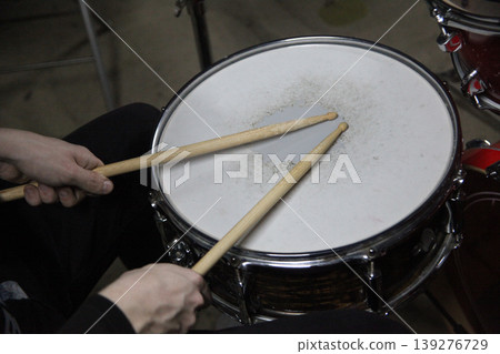 A musician holds drumsticks above a snare drum in a music studio. 139276729