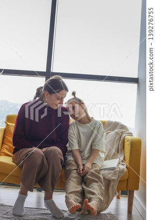 Pretty mother and daughter sitting on couch at home Pretty mother and daughter sitting on couch at home 139276755