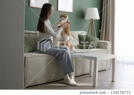 Joyful woman and cat sitting on a couch in a living room Joyful woman and cat sitting on a couch in a living room 139276771