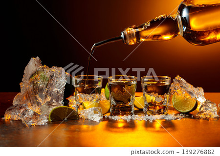 The tequila is poured from the bottle into shot glasses. 139276882