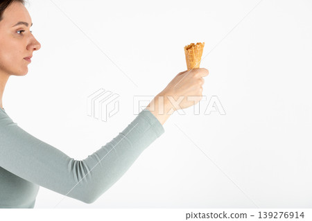Woman holding empty waffle ice cream cone looking left Woman holding empty waffle ice cream cone looking left 139276914