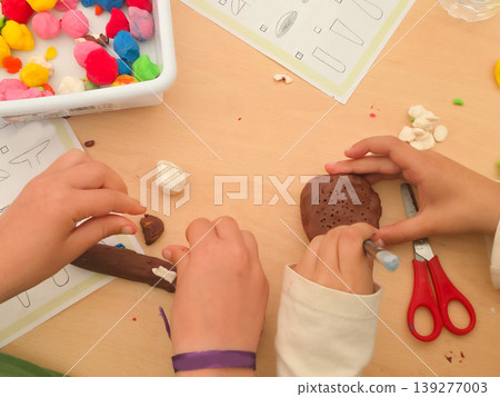 A child molds colorful clay into a mushroom shape at a classroom desk. Concepts of creativity, tactile learning, and child development through play. A child molds colorful clay into a mushroom shape at a classroom desk. Concepts of creativity, tactile learning, and child development through play. 139277003