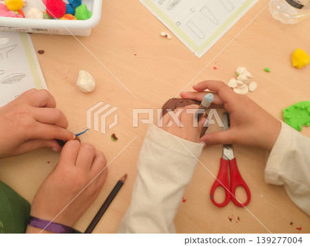 A child molds colorful clay into a mushroom shape at a classroom desk. Concepts of creativity, tactile learning, and child development through play. A child molds colorful clay into a mushroom shape at a classroom desk. Concepts of creativity, tactile learning, and child development through play. 139277004