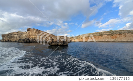 One isolated small rock stands in the sea in front of the rocky coast 139277115