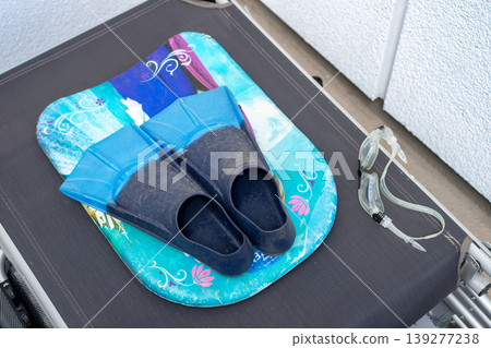 Fins,goggles and a swimming board covered in dust lie on an assembled deck chair Fins,goggles and a swimming board covered in dust lie on an assembled deck chair 139277238