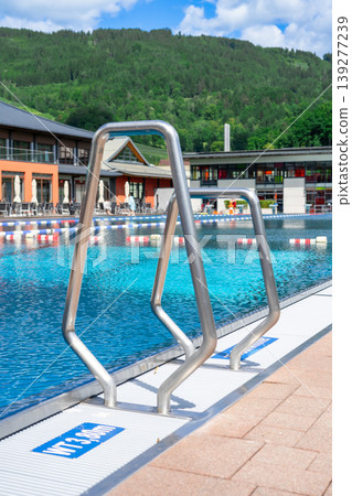 Handrails of stairs in an outdoor public swimming pool with turquoise water Handrails of stairs in an outdoor public swimming pool with turquoise water 139277239