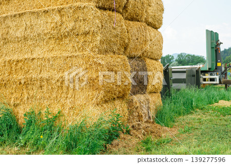 Piles of hay stacked on top of each other with farm equipment in the background Piles of hay stacked on top of each other with farm equipment in the background 139277596