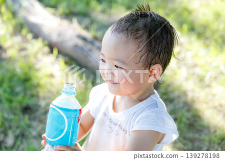 一張夏日寫真，照片中一個蹣跚學步的孩子麵帶微笑，正在喝水。 139278198