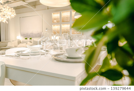 A modern dining table setting featuring white tableware and wine glasses. 139279644