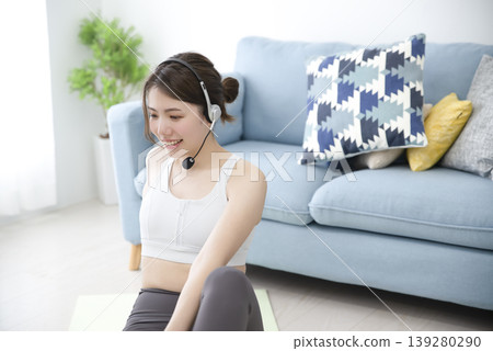 A woman wearing a headset is streaming online yoga from her home. A woman wearing a headset is streaming online yoga from her home. 139280290