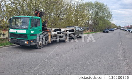 Green flatbed truck parked on a gravel lot near a forest, long haul transport logistics, automotive industry Green flatbed truck parked on a gravel lot near a forest, long haul transport logistics, automotive industry 139280536