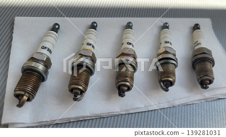 Used automotive spark plugs arranged on a white surface, car engine maintenance, mechanical repair service, industrial workshop kit Used automotive spark plugs arranged on a white surface, car engine maintenance, mechanical repair service, industrial workshop kit 139281031