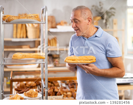 Senior male customer stands with croissant in hands near window of bakery. 139281456