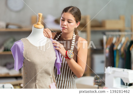 Female tailor sews new dress on a mannequin in sewing studio Female tailor sews new dress on a mannequin in sewing studio 139281462