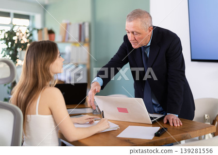 Young woman working in team with mature man, they sitting at table Young woman working in team with mature man, they sitting at table 139281556